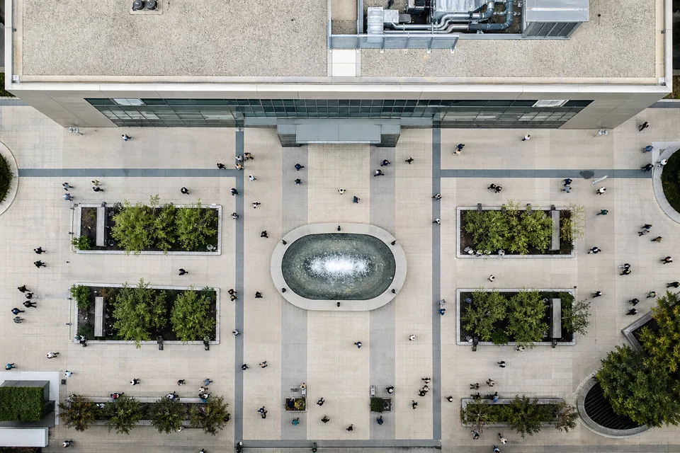 Drone view straight down on a plaza in front of a corporate headquarters with small anonymous figures crossing it