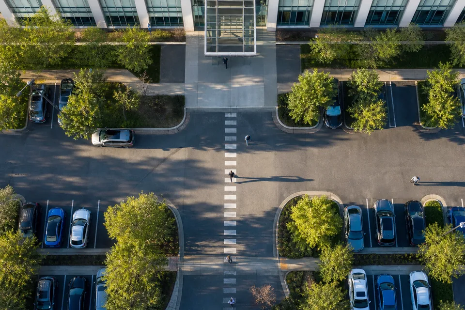 Drone view straight down on an office campus parking lot filling up in the morning, small figures walking to the entrance