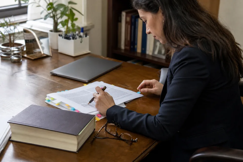 In-house counsel marking a printed contract page with a fountain pen on a desk with sticky flags and a legal reference book