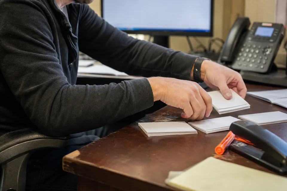 Hands of a sales manager sorting printed index cards into three piles on a desk with an orange marker