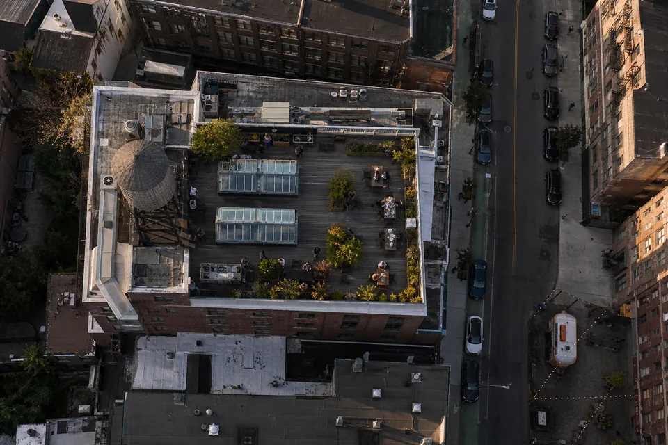 Drone view straight down on a converted brick warehouse block with a rooftop deck, skylights and a narrow street with parked cars