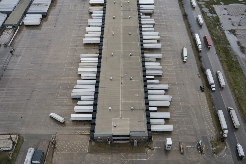 Drone view straight down on a logistics cross-dock terminal with dozens of trailers parked at the doors and a yard tractor moving between them