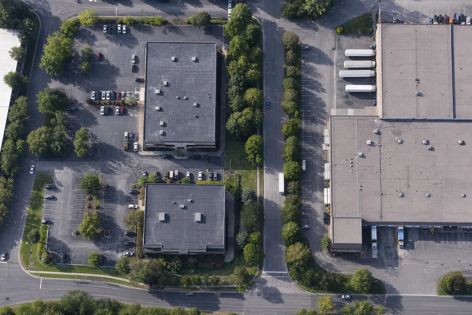Drone view straight down on a US business park with office buildings, a warehouse with trucks at the dock, tree lines and a half-full parking lot