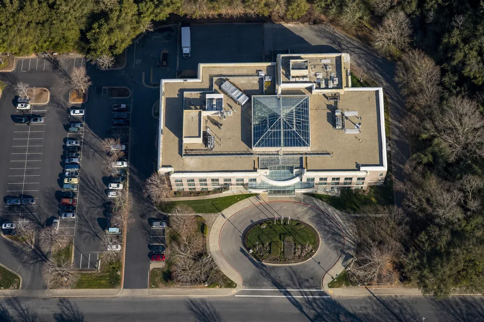Drone view straight down on a single company headquarters, a four-storey office with a glass atrium roof, its parking lot and the access road